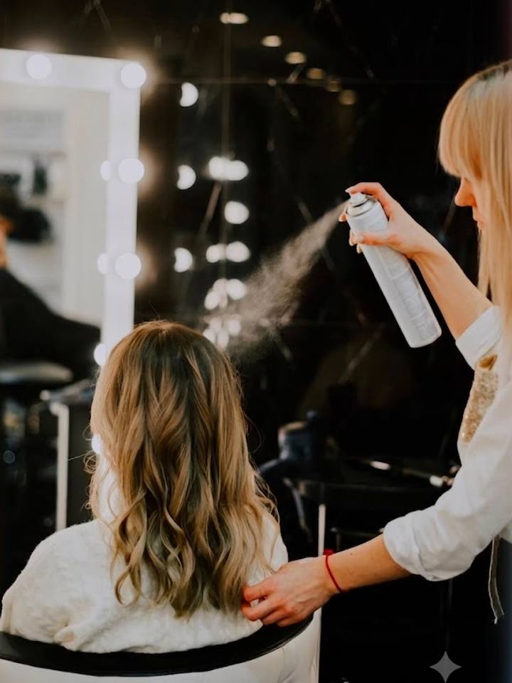 Stylist finishing a client's waves with setting spray in front of a mirror